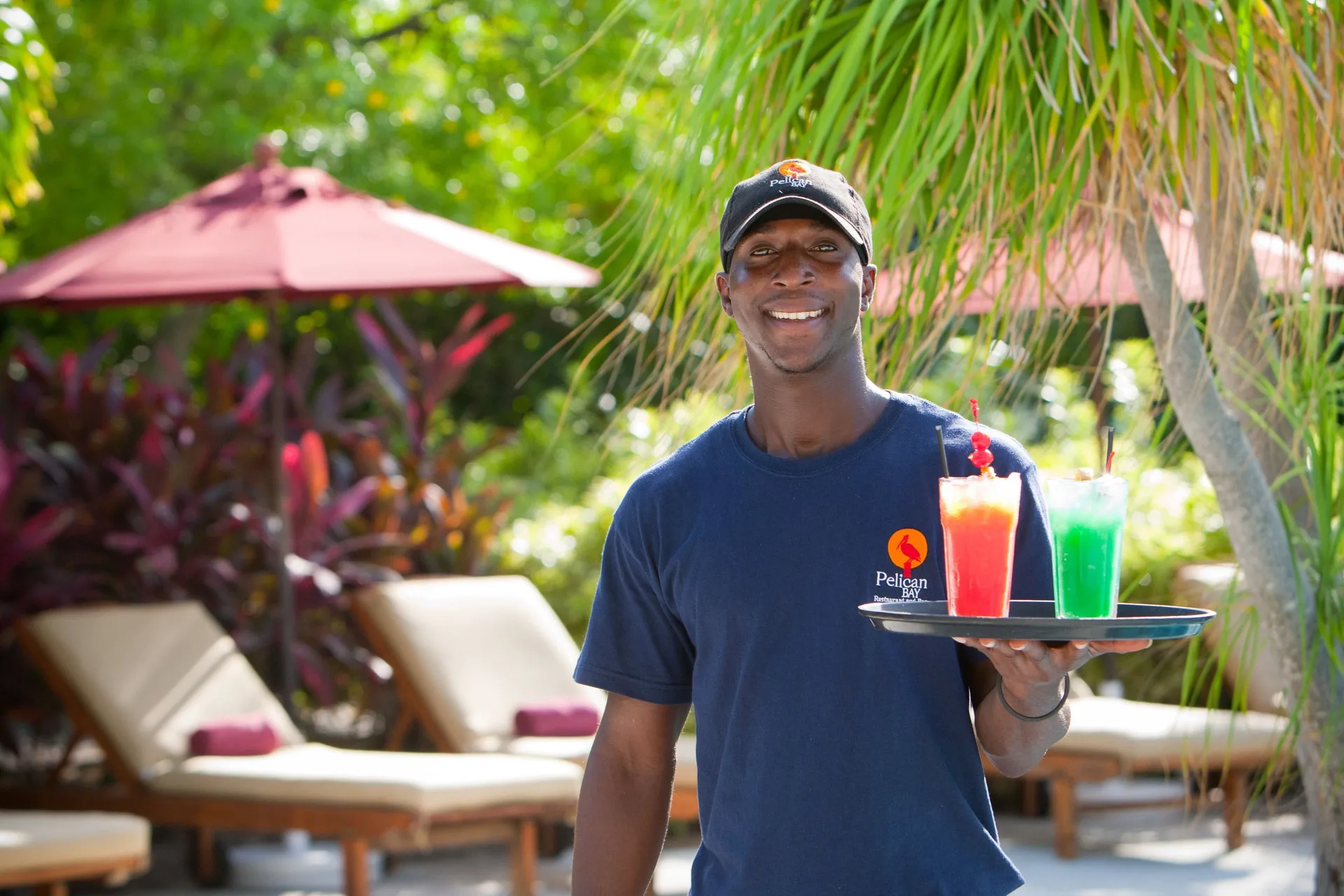 Server holding two colorful drinks by lounge chairs at Royal West Indies Resort.