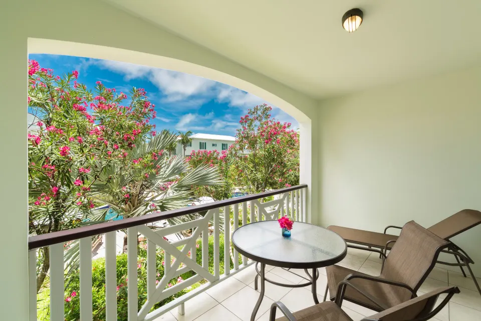 Studio Botanical View covered balcony with table, chairs, lounger and flowering trees at Royal West Indies Resort.