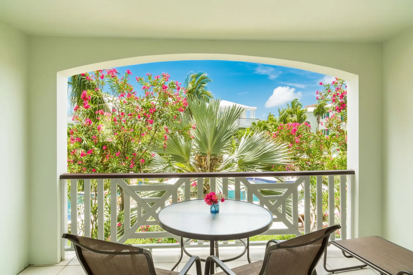 Studio Botanical View balcony table and chairs facing palms and pink blossoms at Royal West Indies Resort.