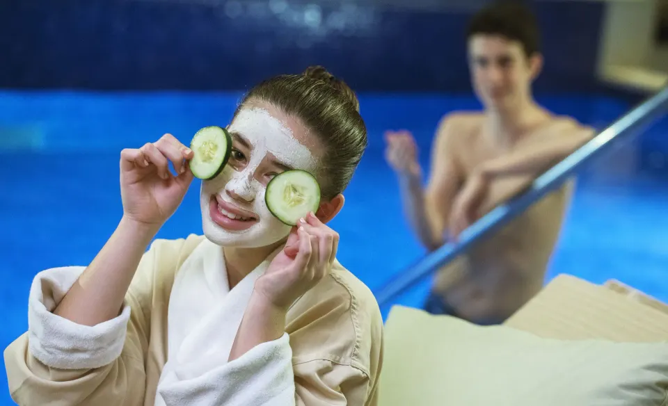 A guest with a facial mask and cucumber slices relaxes by a spa pool at Royalton Bavaro Resort & Casino.