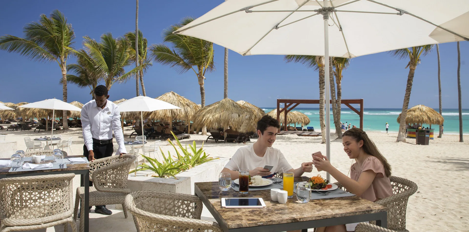 Beachfront dining table with guests and umbrellas at Royalton Bavaro Resort & Casino.