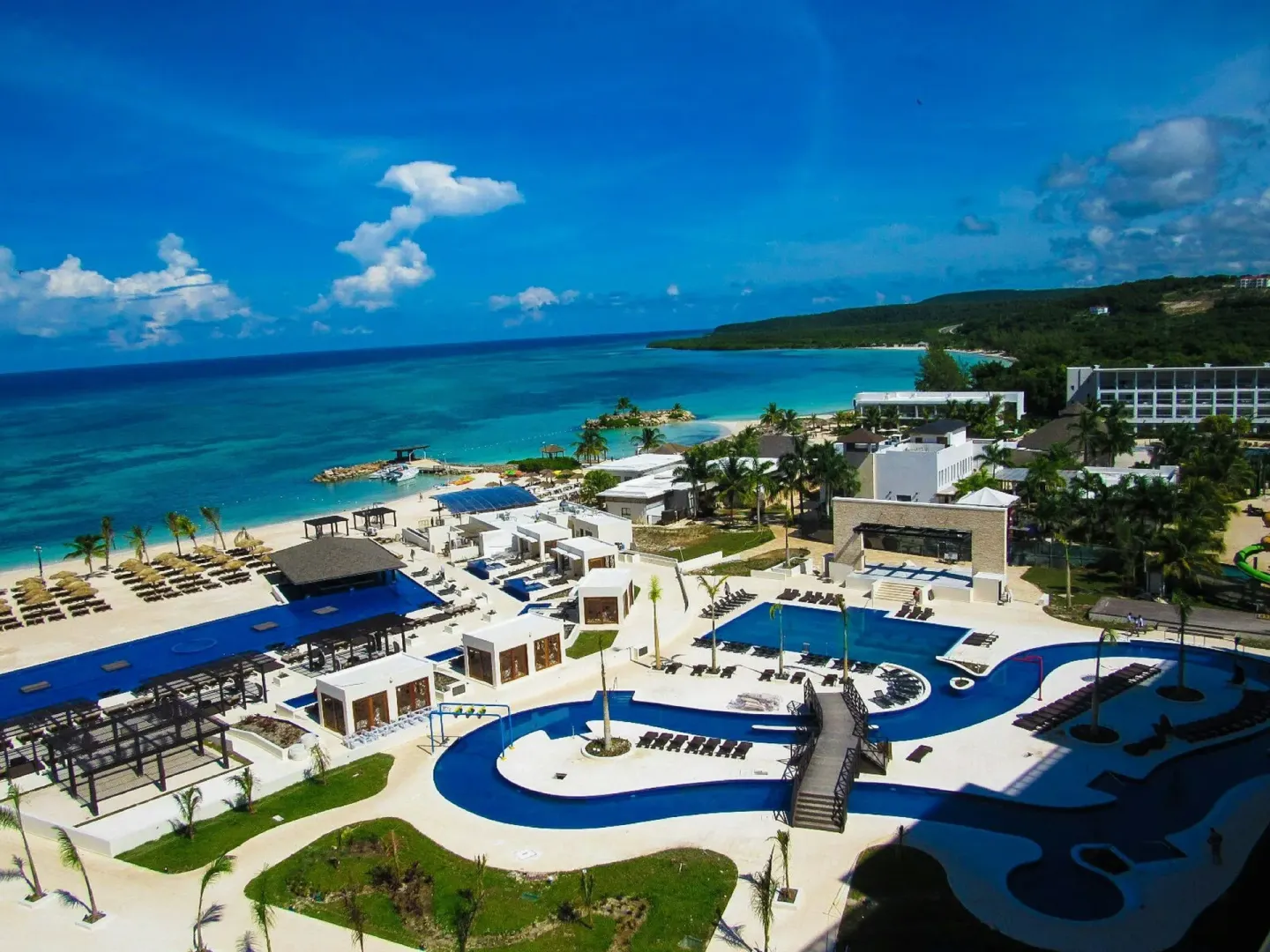 An aerial view shows pools, beach, and turquoise sea at Royalton Blue Waters Montego Bay.