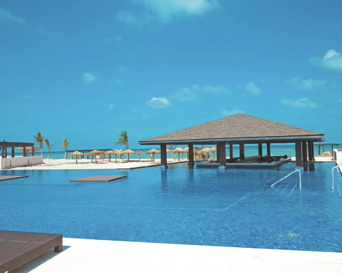 An infinity-style pool faces beach palapas and the sea at Royalton Blue Waters Montego Bay.