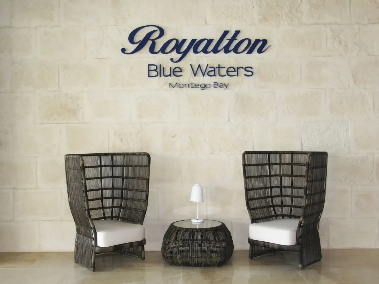 Two wicker lounge chairs sit beneath the wall logo at Royalton Blue Waters Montego Bay.