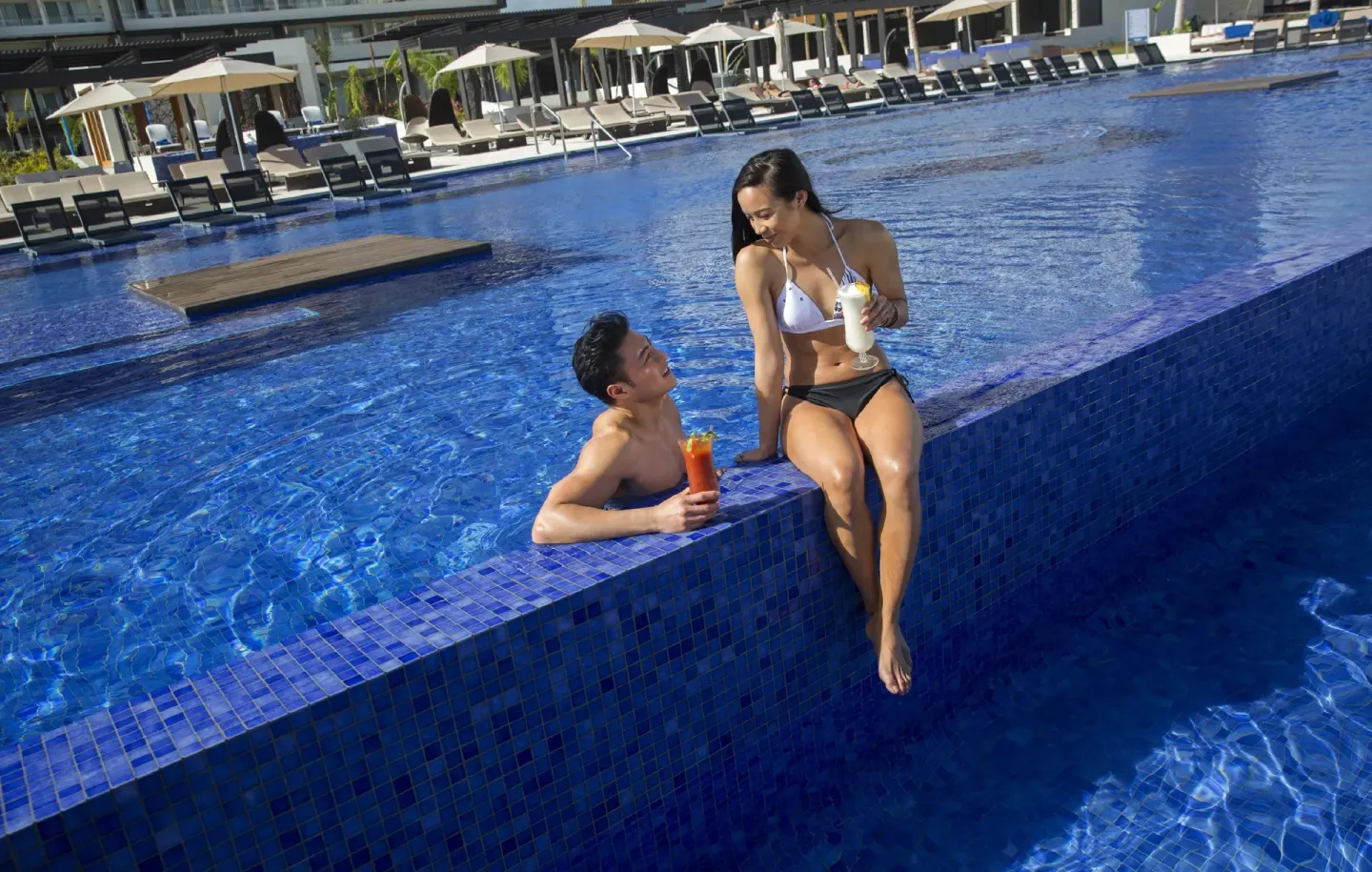 Guests with drinks by the blue swimming pool at Royalton Blue Waters Montego Bay.