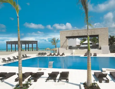 A pool deck with loungers, palms, and an ocean backdrop at Royalton Blue Waters Montego Bay.