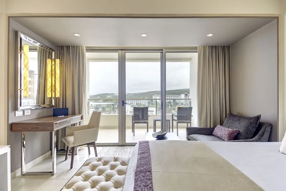 Luxury Junior Suite king bed with desk and balcony at Royalton Blue Waters Montego Bay.