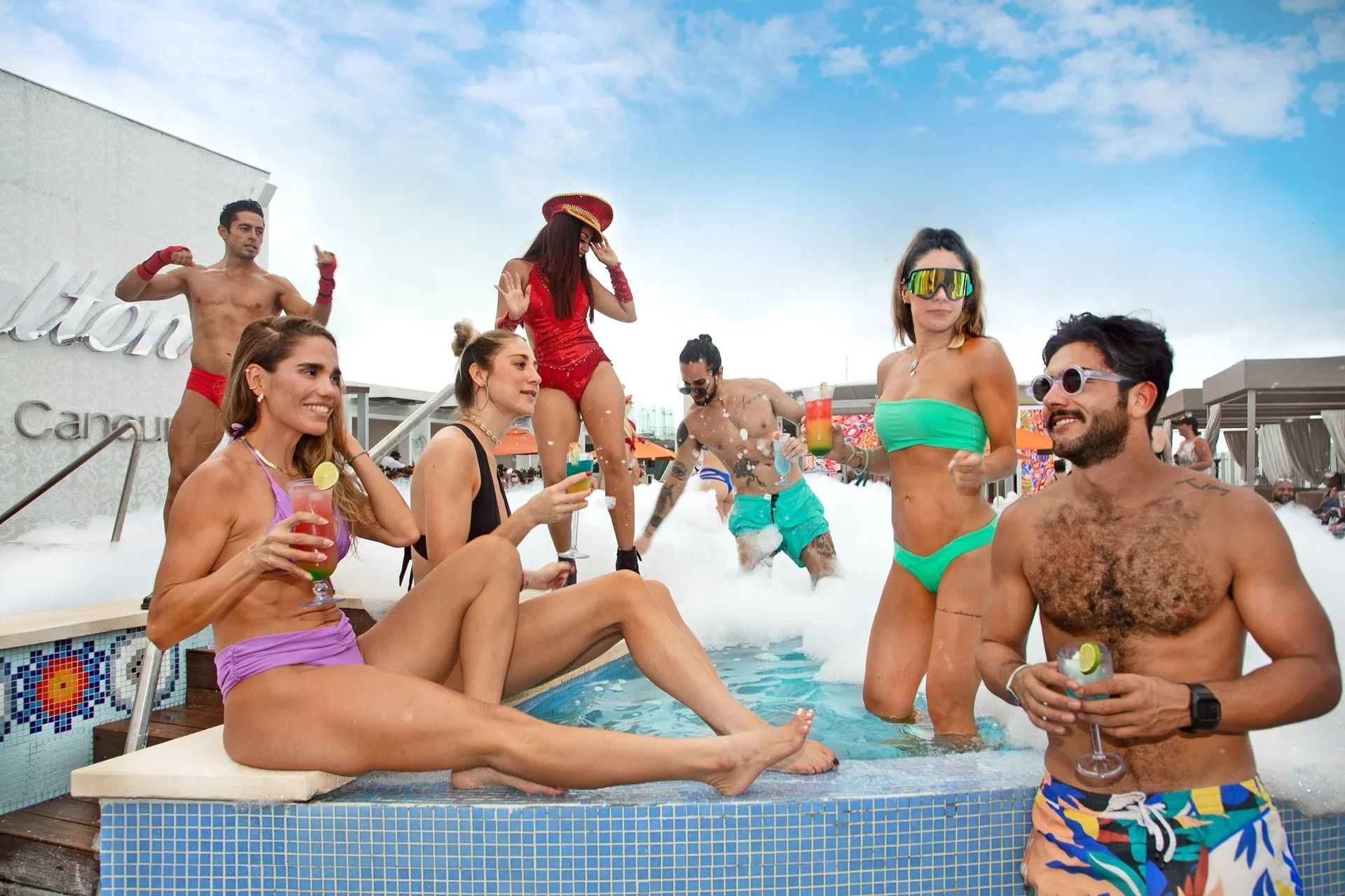 Guests with cocktails gather in a foamy rooftop pool at Royalton CHIC Cancun.