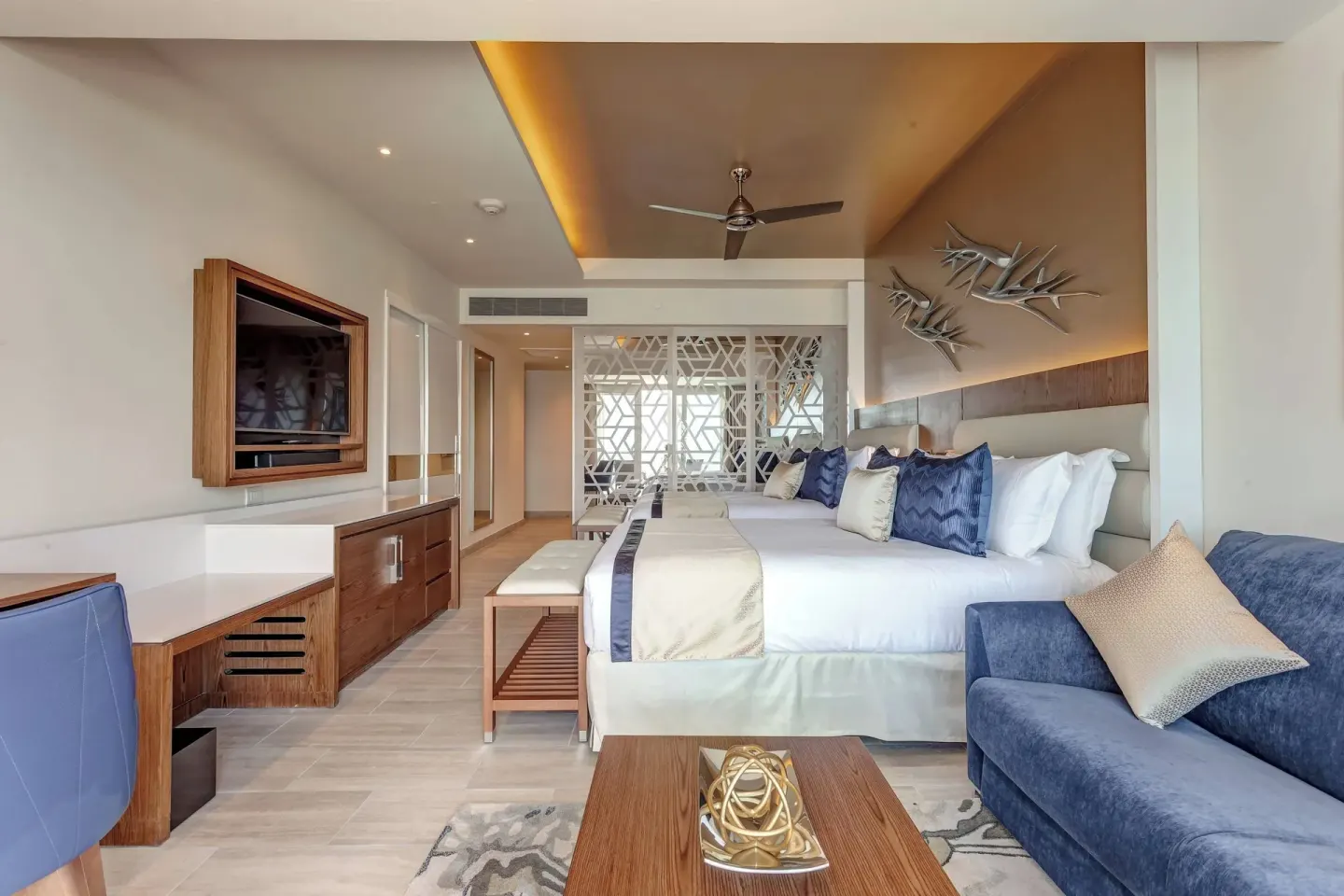 Suite bedroom with king bed, blue sofa, desk and TV at Royalton CHIC Cancun.