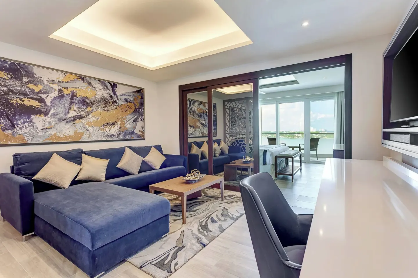 Suite living area with blue sofa, desk and bedroom beyond at Royalton CHIC Cancun.