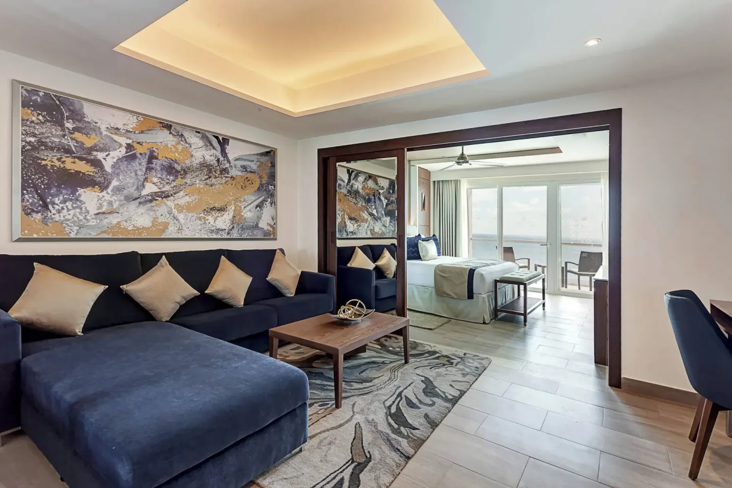 Suite living room with blue sofa opening to a bedroom and balcony at Royalton CHIC Cancun.