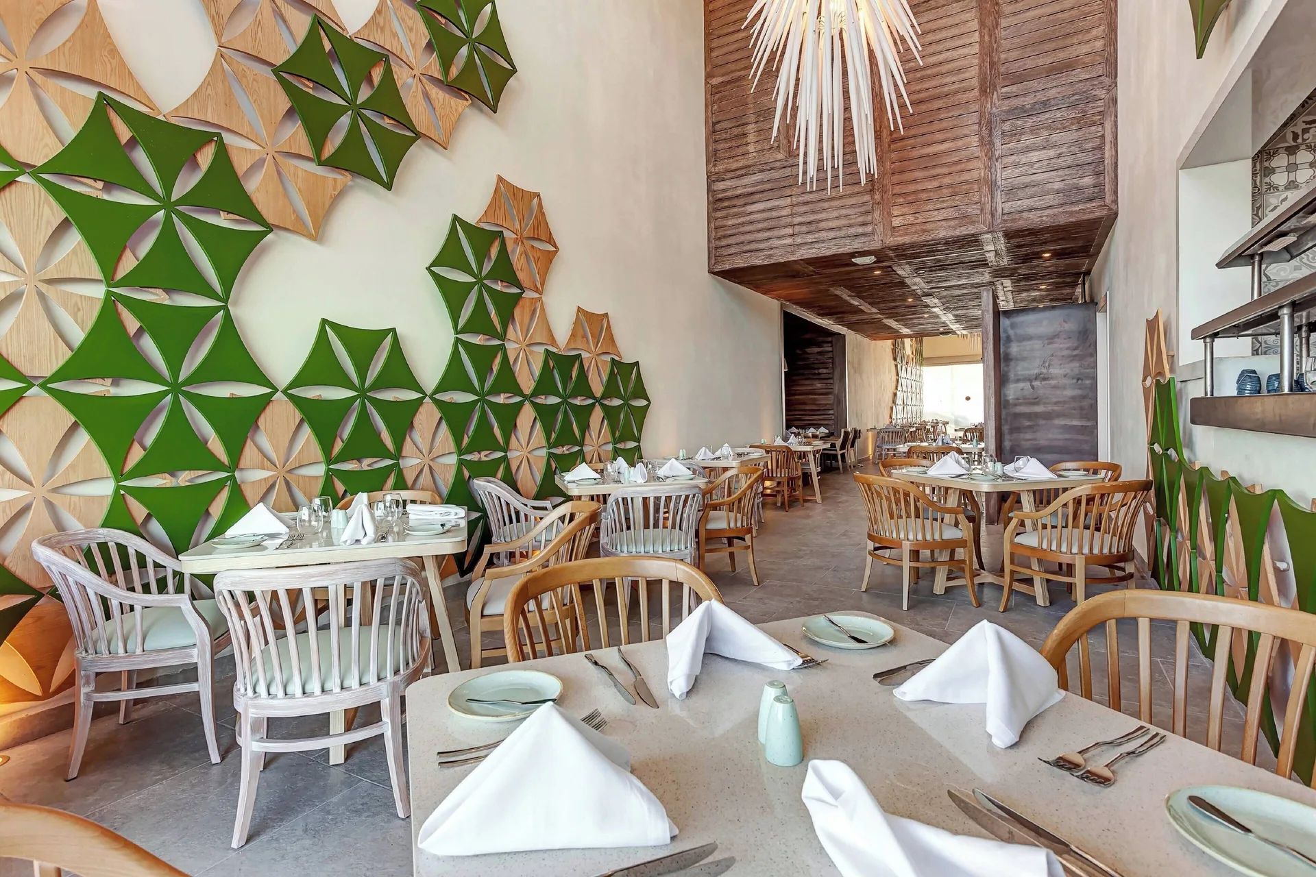 A bright restaurant with green geometric wall art and set tables at Royalton CHIC Cancun.