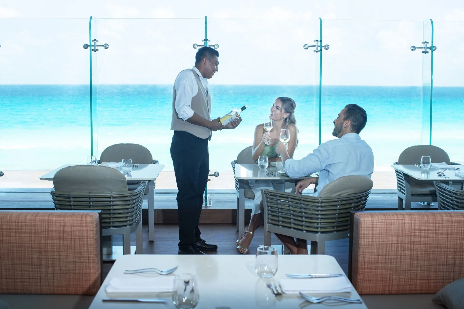 A server presents a wine bottle to guests in an oceanfront dining room at Royalton CHIC Cancun.