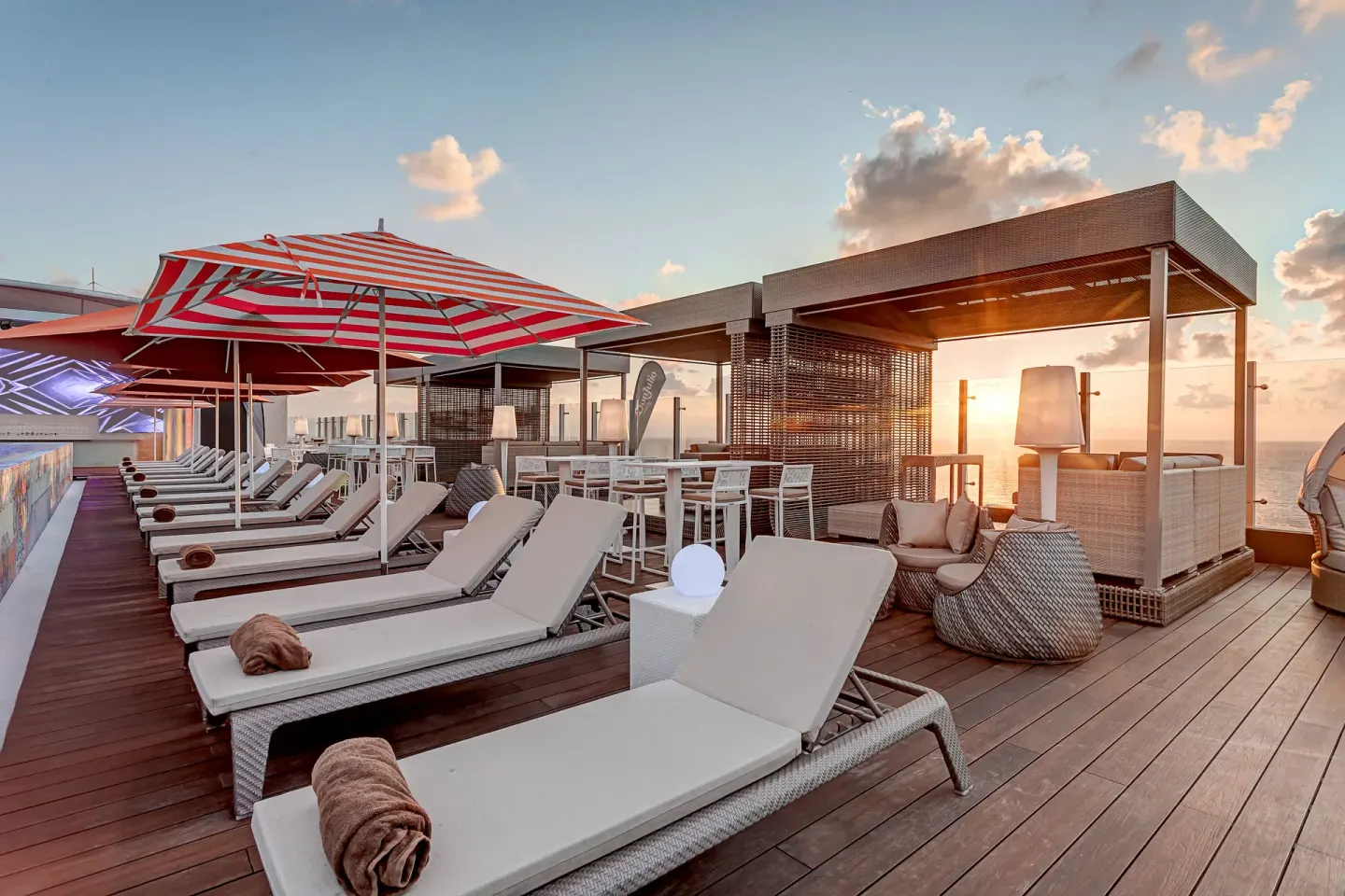Rooftop lounge deck with loungers, striped umbrellas, and sunset views at Royalton CHIC Cancun.
