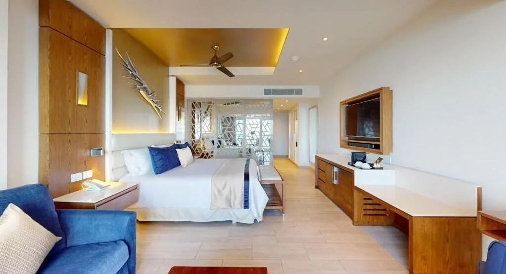 Luxury Suite Sunset View king bed, blue chair, and media console at Royalton CHIC Cancun.