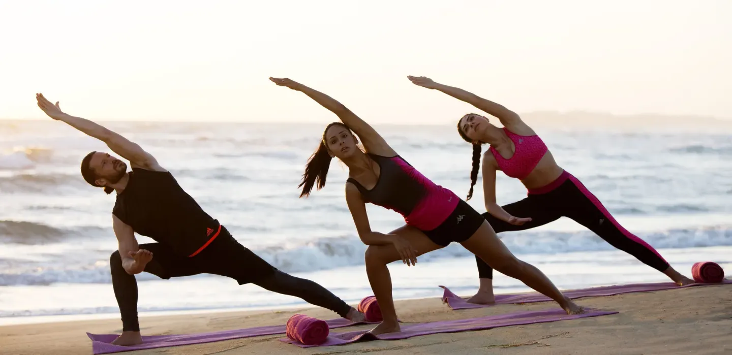 Three guests stretch on beach mats by the ocean at Royalton CHIC Punta Cana Resort & Casino.