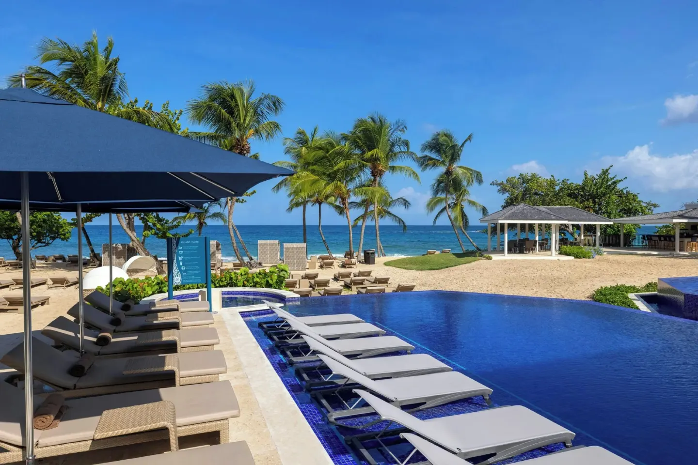 Beachfront pool with loungers, palm trees, and ocean at Royalton Grenada.