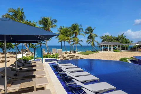 Beachfront pool with loungers, palm trees, and ocean at Royalton Grenada.