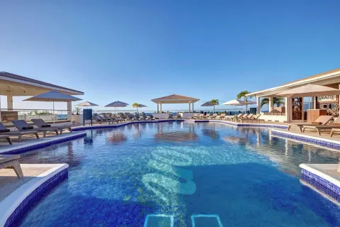 Main pool with loungers, umbrellas, ocean backdrop, and Grazie sign at Royalton Grenada.