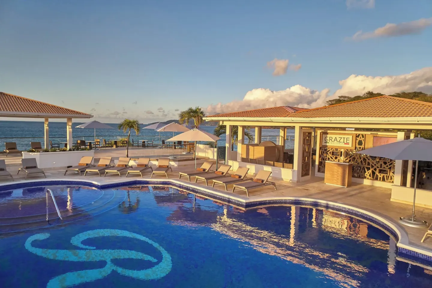 Pool deck beside Grazie restaurant with ocean views at Royalton Grenada.