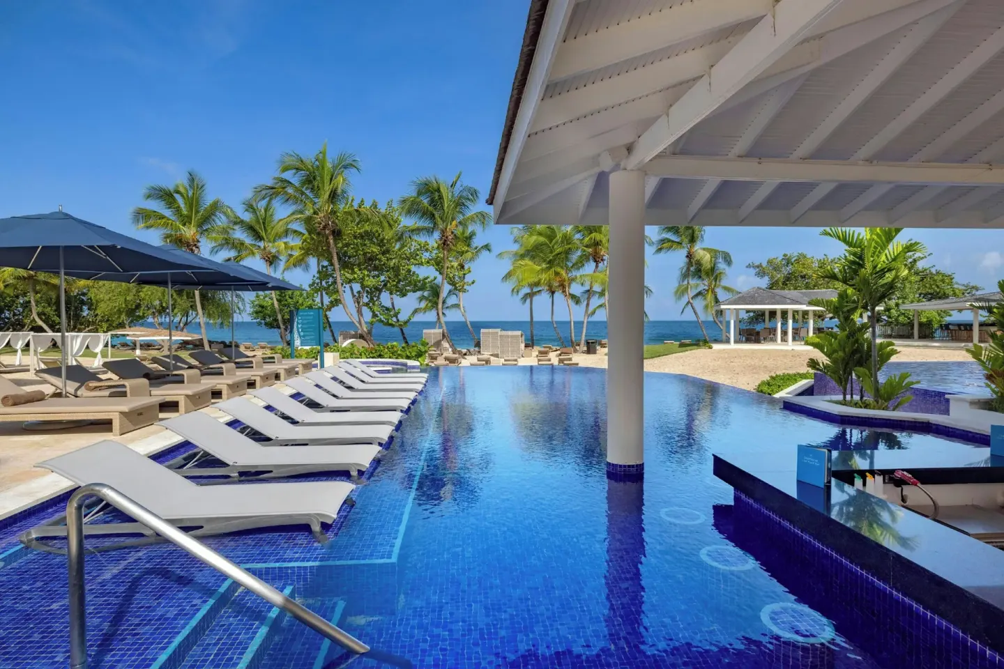 Pool with in-water loungers, palms, and ocean beyond at Royalton Grenada.