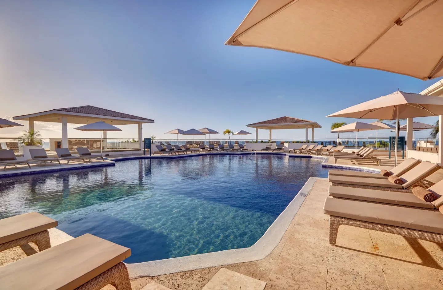 Sunny pool terrace with loungers, umbrellas, and ocean horizon at Royalton Grenada.