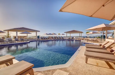 Sunny pool terrace with loungers, umbrellas, and ocean horizon at Royalton Grenada.
