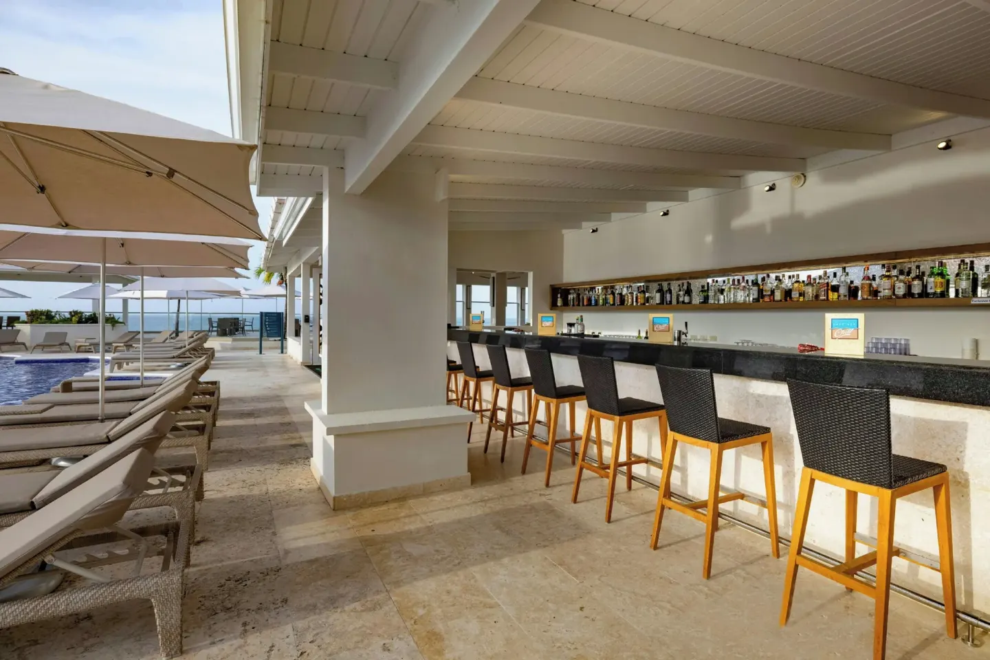 Covered poolside bar with stools and bottles at Royalton Grenada.