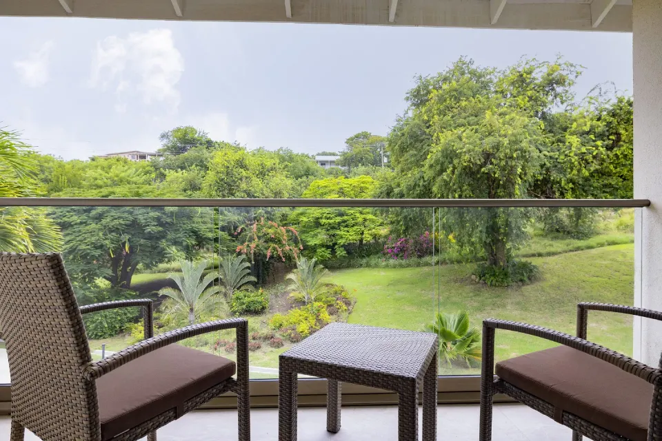 Luxury Room balcony at Royalton Grenada with two woven chairs, a table, and garden views.