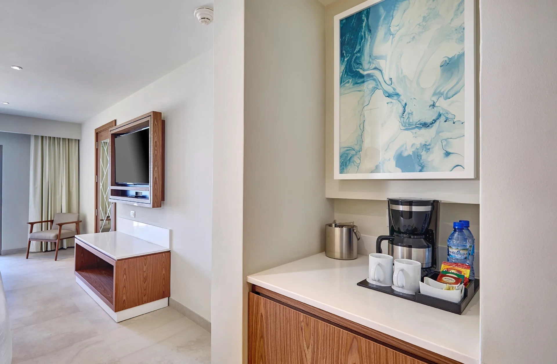 Luxury Room refreshment counter at Royalton Grenada with coffee maker, cups, water, and TV beyond.