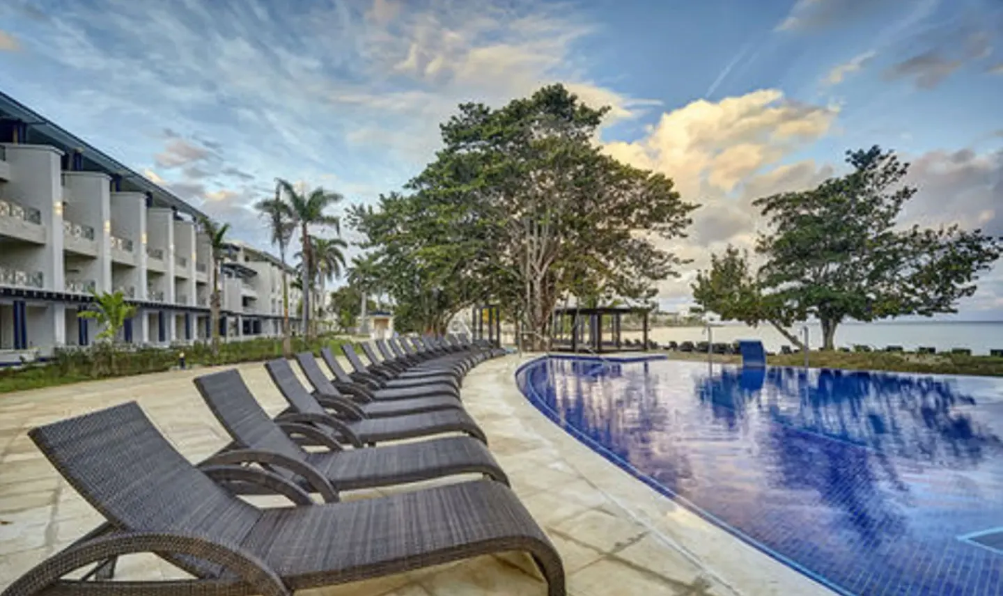 Chaise lounges face a curved pool beside the guest building at Royalton Hideaway Negril.
