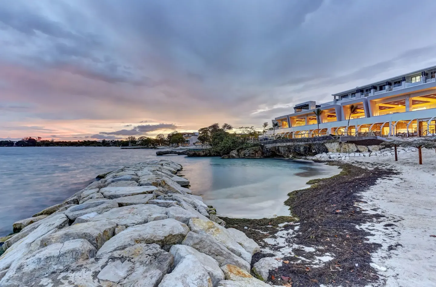 Rock jetty, small beach cove and lit waterfront buildings at Royalton Hideaway Negril.
