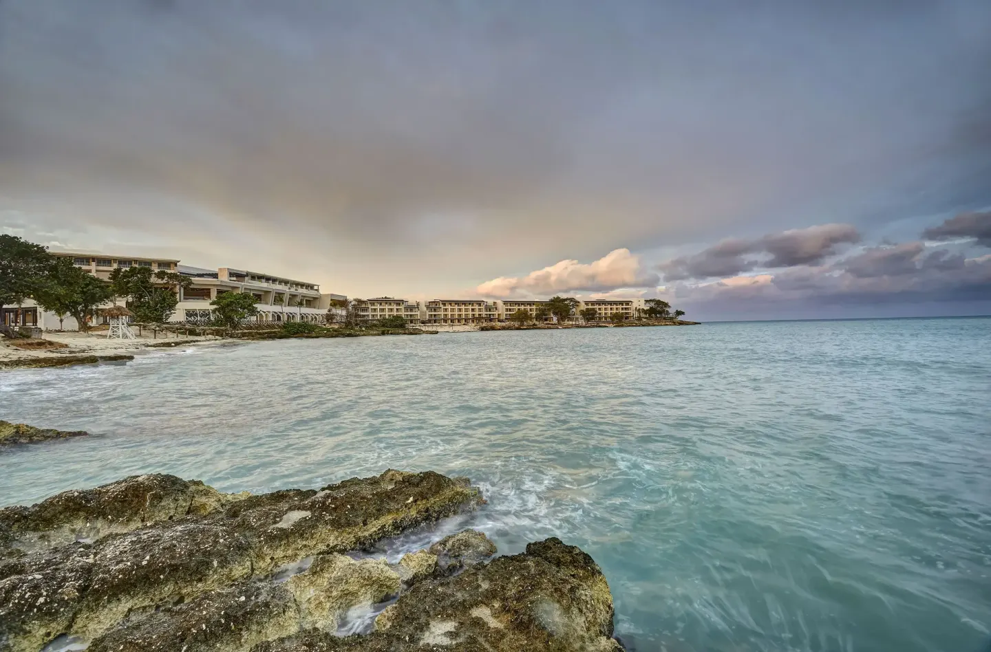 Rocky foreground, turquoise sea and distant resort buildings at Royalton Hideaway Negril.