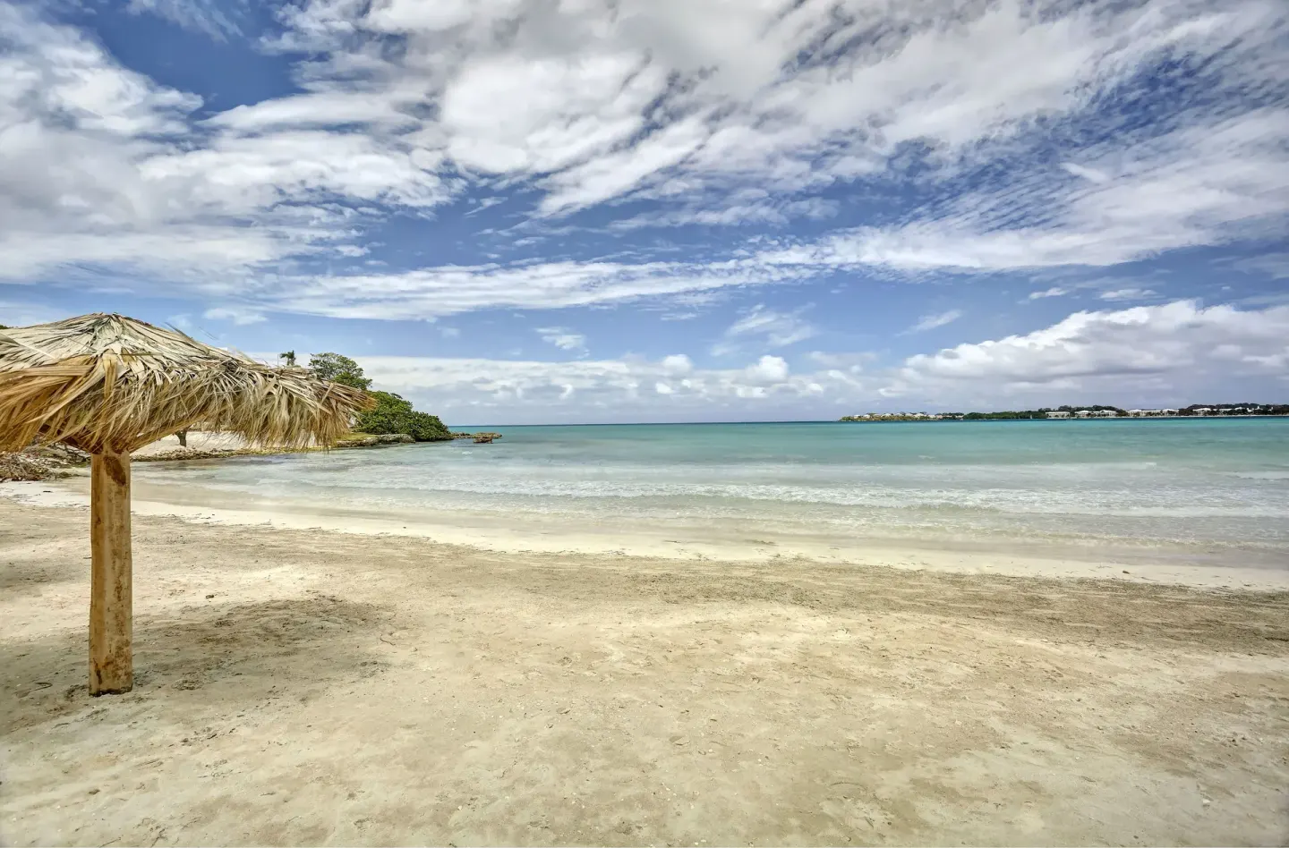 Sandy beach with a thatched umbrella and calm water at Royalton Hideaway Negril.