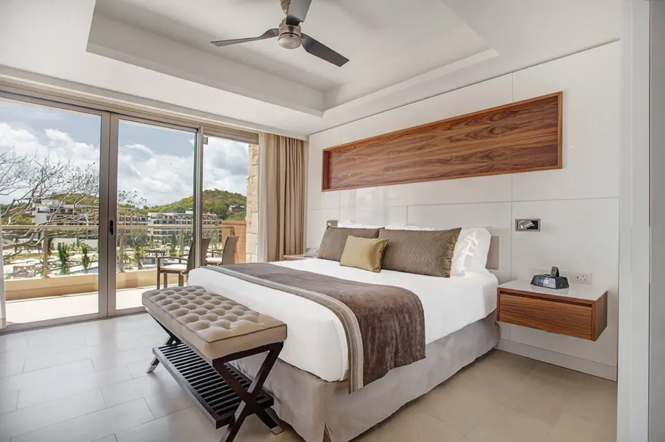 Luxury Junior Suite Ocean View king bed beside balcony doors at Royalton Hideaway Negril.
