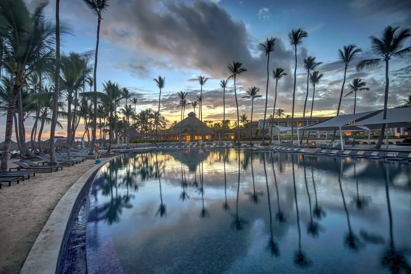 Sunset over the main pool and palm trees at Royalton Hideaway Punta Cana Resort & Casino.
