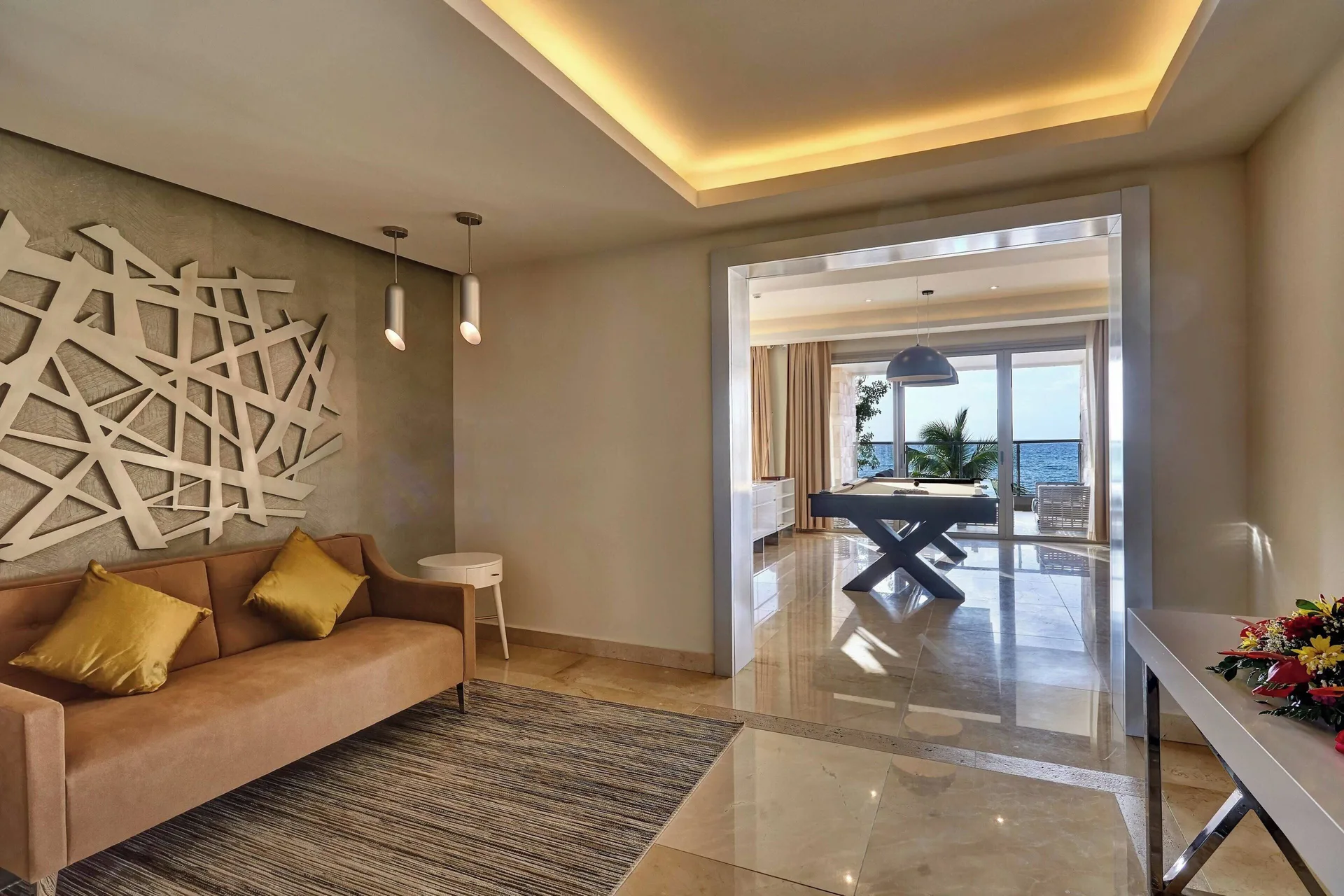 Suite sitting area with sofa and game room beyond at Royalton Hideaway Saint Lucia.