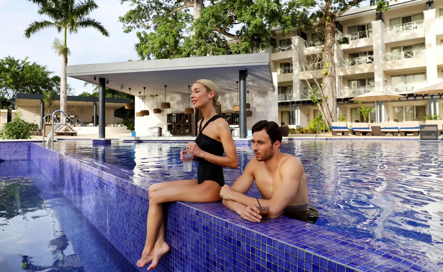 Couple relaxing with drinks in a blue-tiled pool at Royalton Negril.