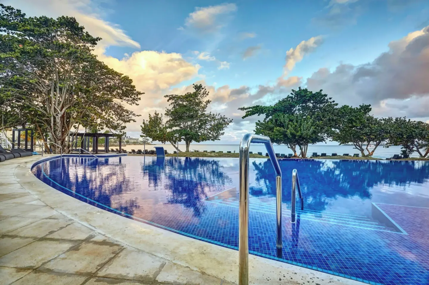 Curved pool with handrails and ocean beyond at Royalton Negril.