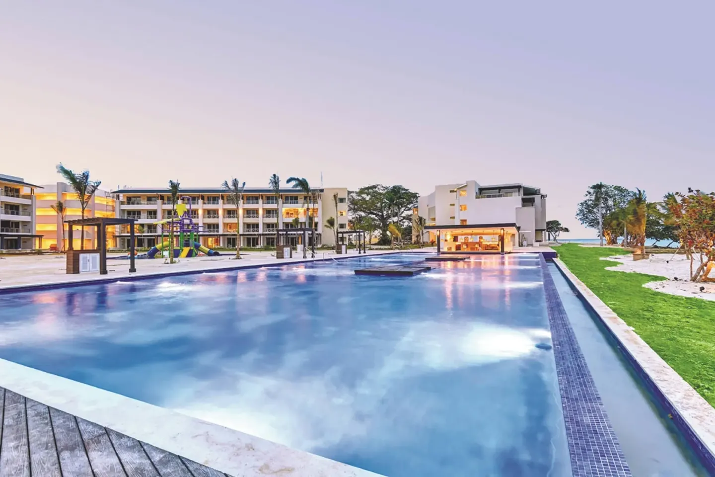 Large pool with resort buildings, splash area, and beach edge at Royalton Negril.