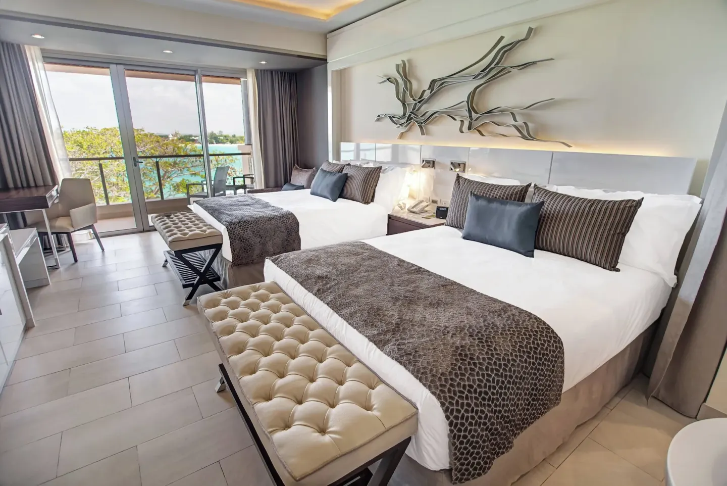 Two beds and balcony doors with ocean visible in a Royalton Negril suite bedroom.