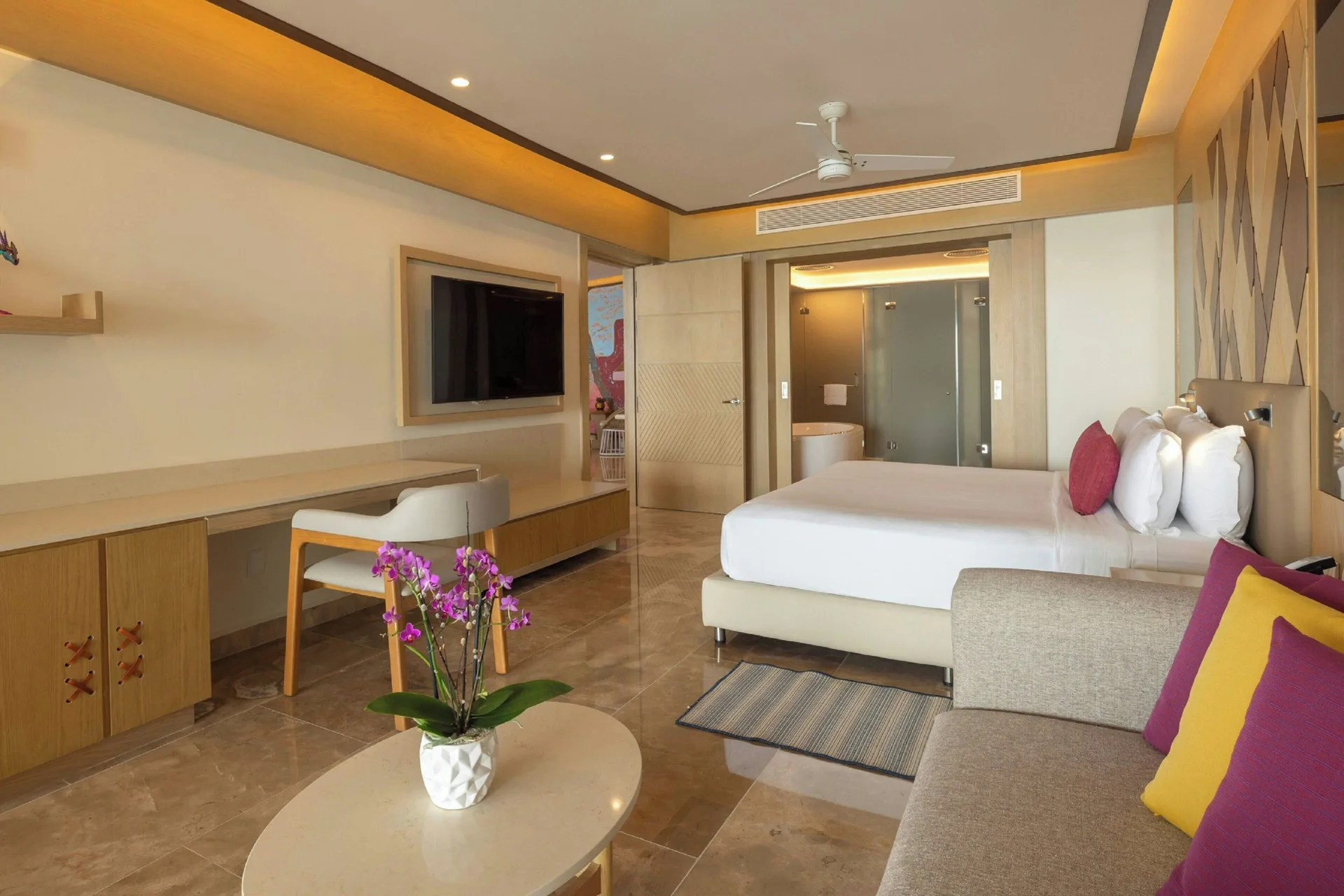 King-bed guest room with sofa, desk, and bathroom at Royalton Splash Riviera Cancun.