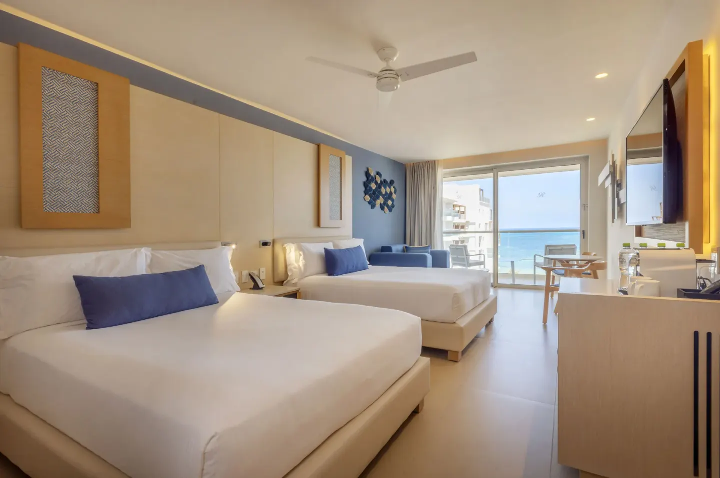 Two-bed oceanfront suite at Royalton Splash Riviera Cancun with balcony, sofa, TV, and blue accents.