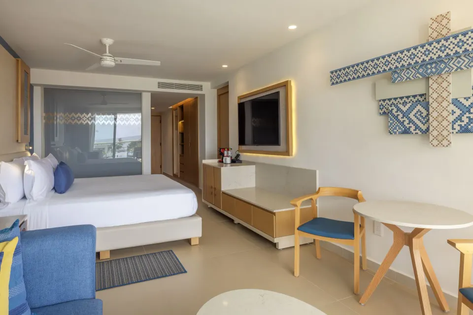 Two Bedroom Luxury Junior Suite bed, sofa, dining nook and TV at Royalton Splash Riviera Cancun.