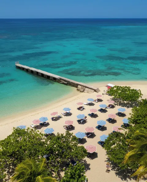 Aerial beach view with pier, umbrellas, and turquoise water at S Hotel Montego Bay.