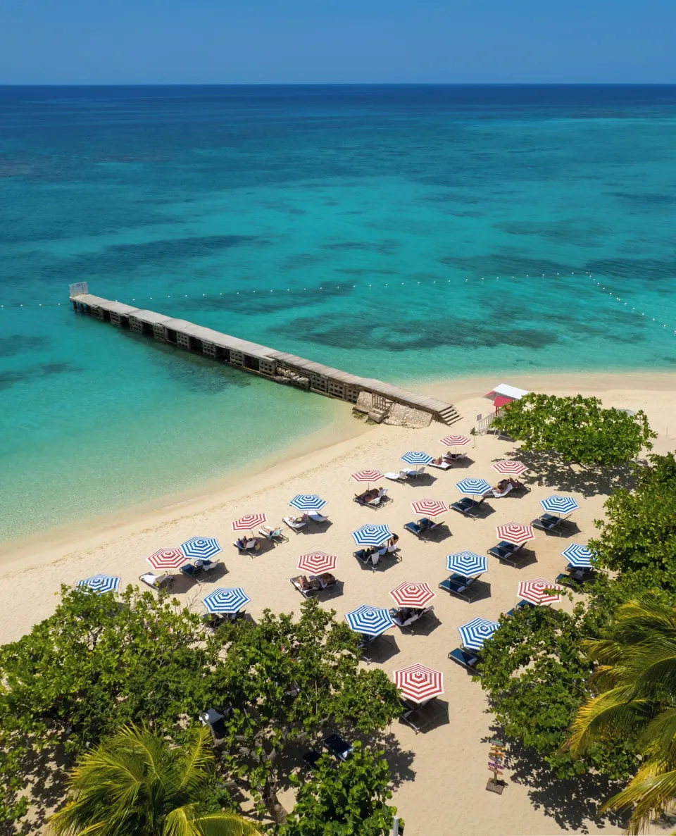 Aerial beach view with pier, umbrellas, and turquoise water at S Hotel Montego Bay.