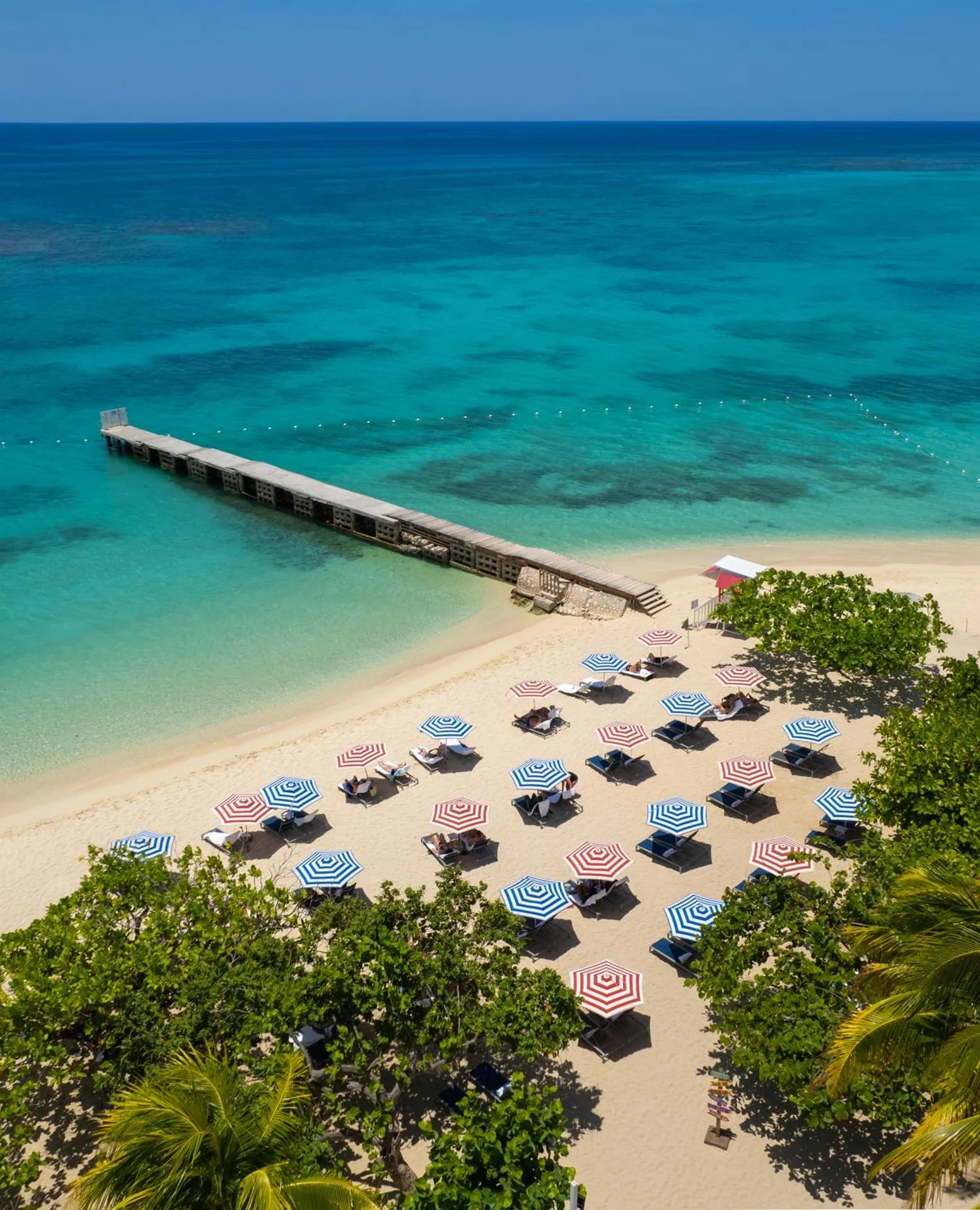 Beach with striped umbrellas, loungers and a pier at S Hotel Montego Bay.