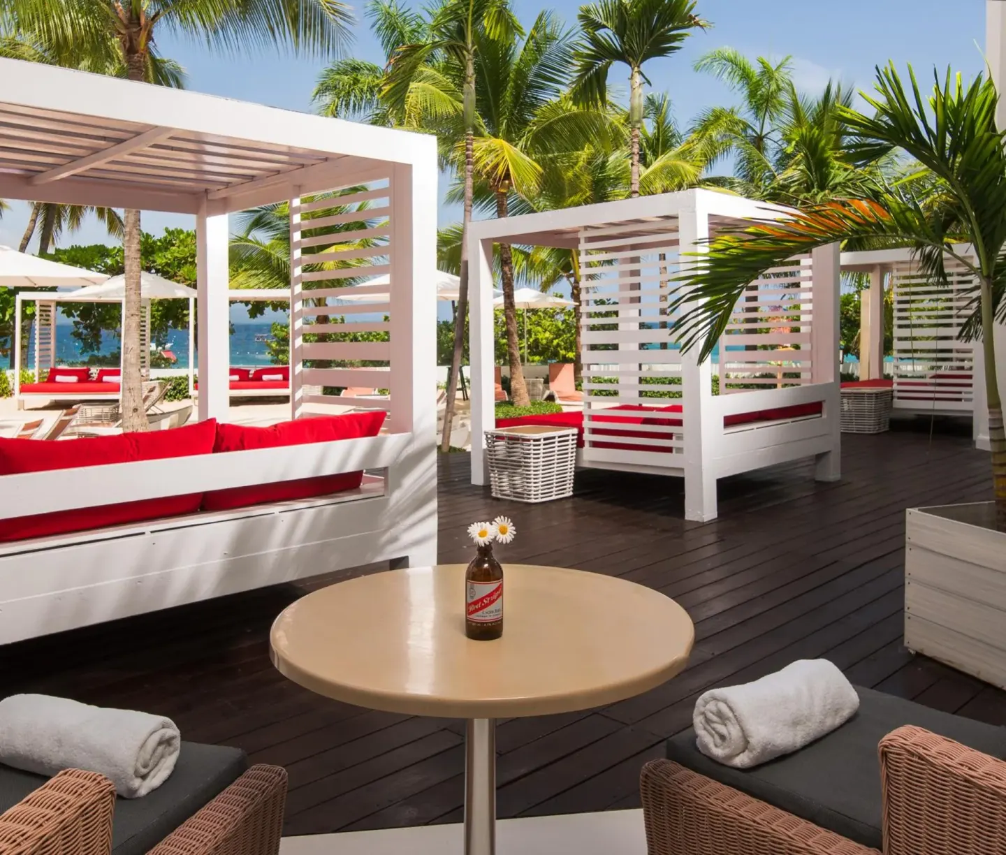 Beachside cabanas with red cushions and palm trees at S Hotel Montego Bay.