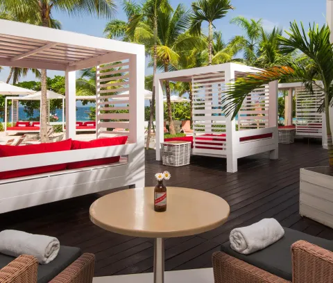 Beachside cabanas with red cushions and palm trees at S Hotel Montego Bay.