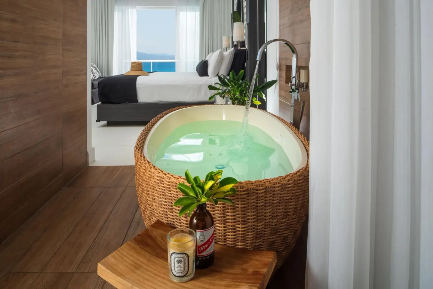 Woven soaking tub with water running beside a guest room bed at S Hotel Montego Bay.